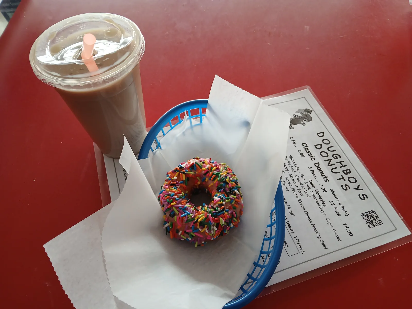 An iced coffee next to a sprinkle donut in a basket and the Doughboys menu