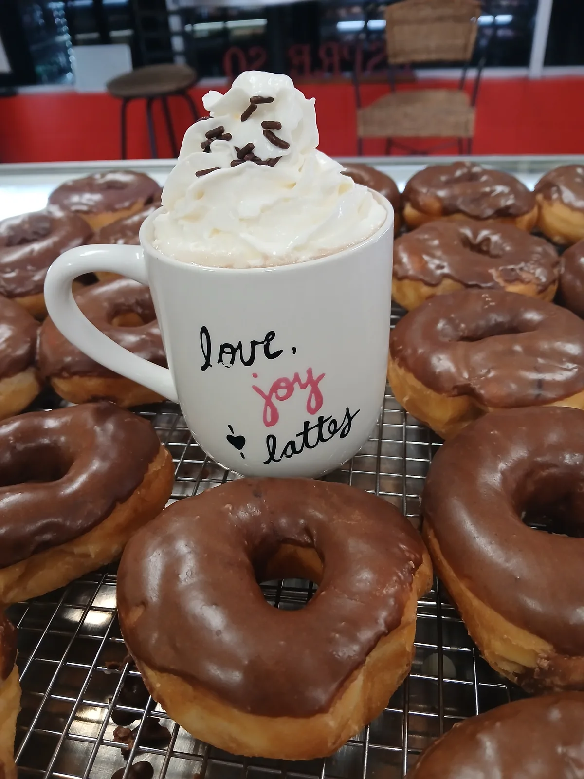 A latte topped with whipped cream and chocolate sprinkles, surrounded by chocolate iced donuts at Doughboys Donuts