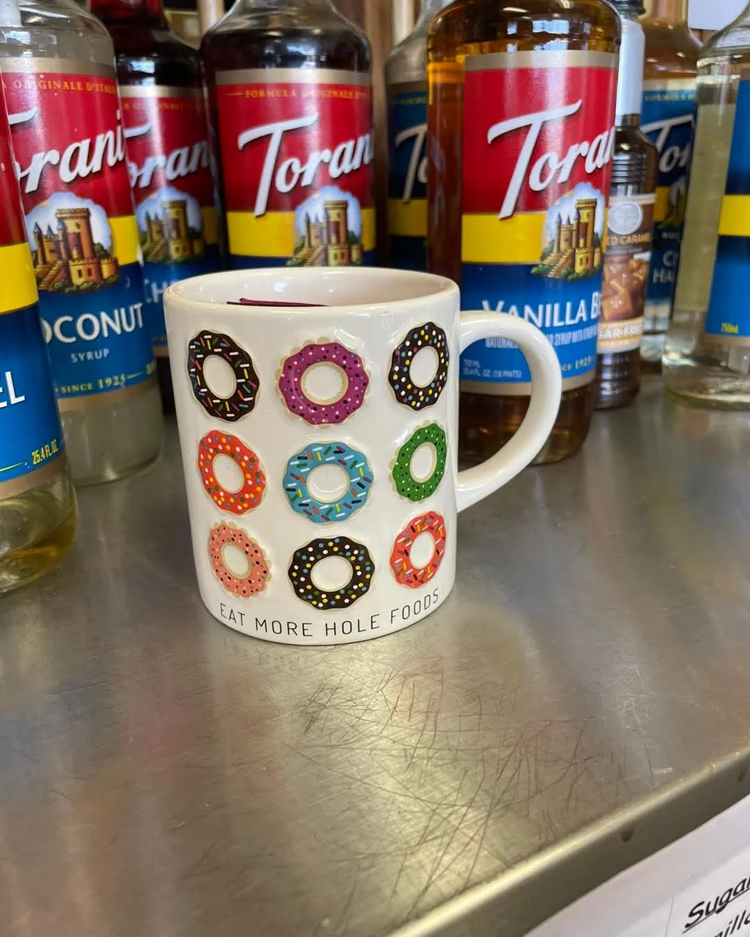 A Doughboys coffee mug in front of the shop's wall of syrup flavor bottles